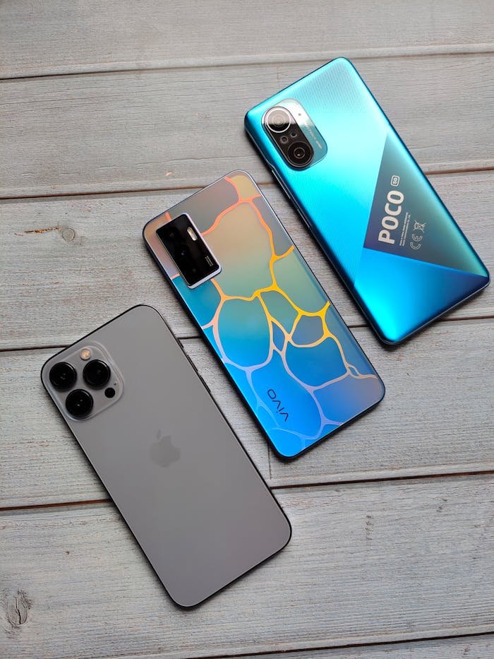 Three different smartphones placed on a wooden surface, highlighting their sleek designs.